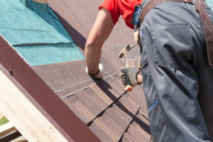 Roofer installing brown asphalt roofing shingles