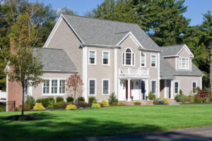 A large, suburban home with a grey shingle roof, grey siding, and a green lawn