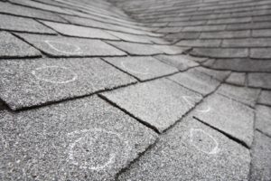 Close-up view of roofing shingles with chalk circles marking damage.