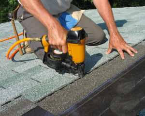 Roofers uses nail gun to attach asphalt shingles to roof