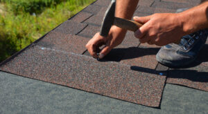 Roofer nailing down asphalt roofing shingles 